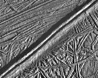 B/W Galileo image of the surface of Europa showing close-spaced parallel cracks in blocks with different orientations, separated by a high ridge furrowed in its center.